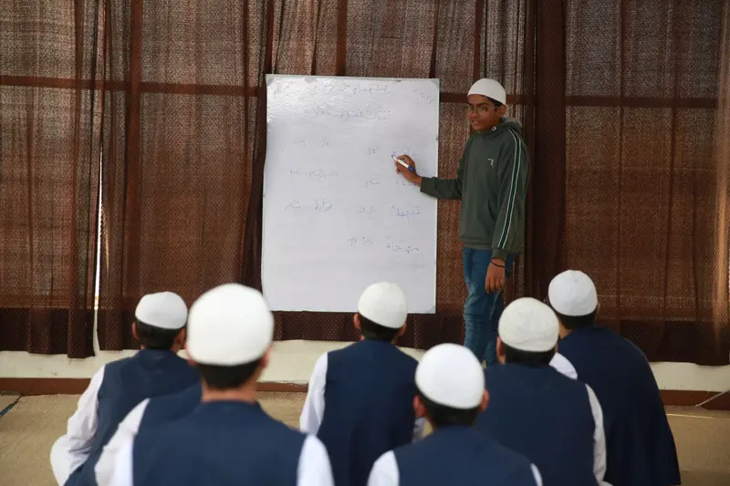 A student writing Arabic on a whiteboard while other students watch