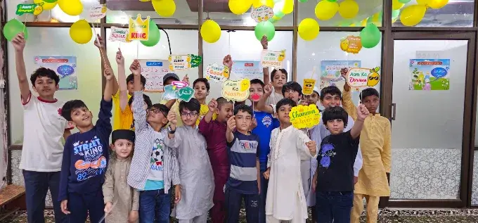 Children holding up colourful paper signs at an indoor academy activity, with balloons behind them