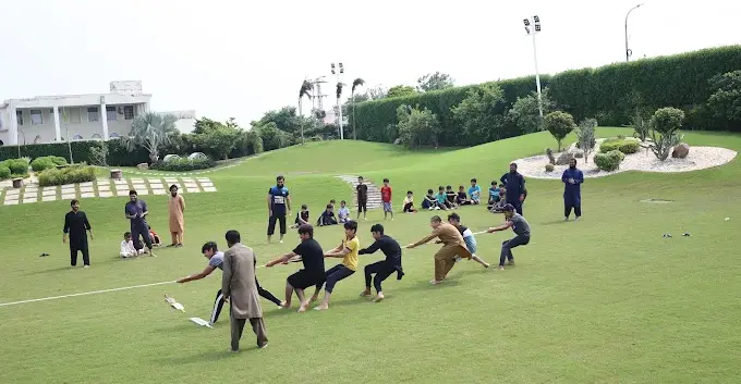 Students and staff playing tug of war on the grass in the academy grounds