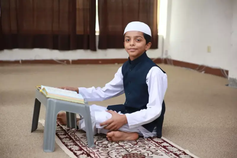 A student in Noon Islamic Academy uniform sitting on a prayer mat with a Quran on a low desk